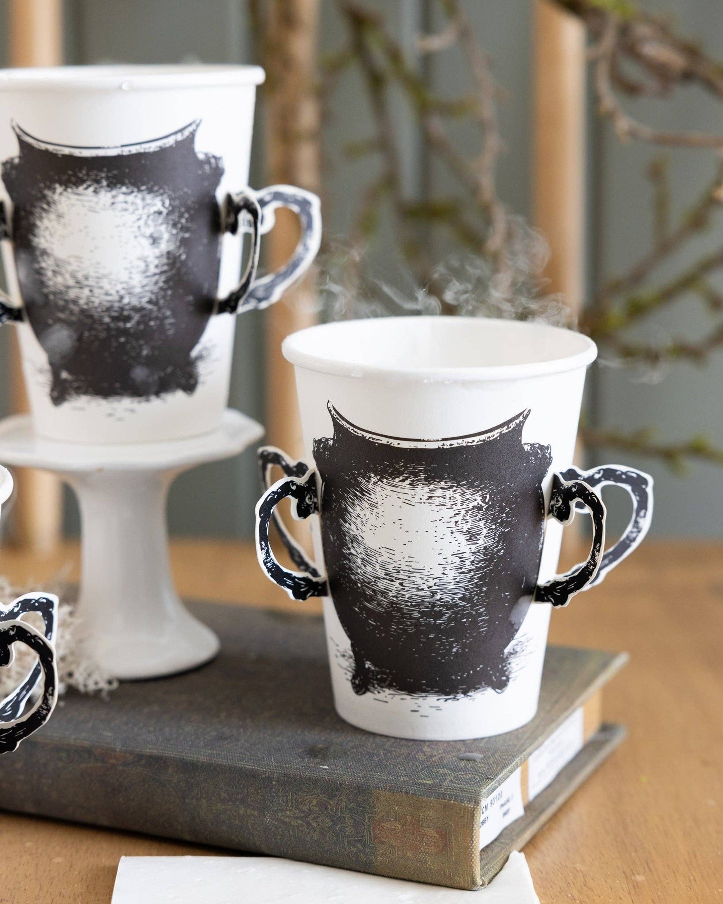 Decorative black and white cauldron paper cups on a wooden surface with a blurred background