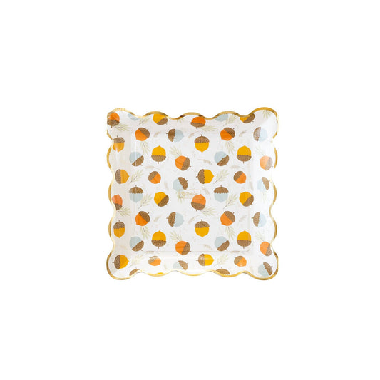 A scalloped paper plate with an acorn-scattered print and gold foil trim.