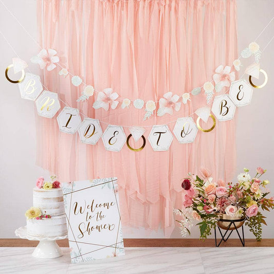 A bridal shower decoration kit displayed, including banners with geometric floral patterns and text, a 'Welcome to the Shower' sign, and a cake with floral decorations.