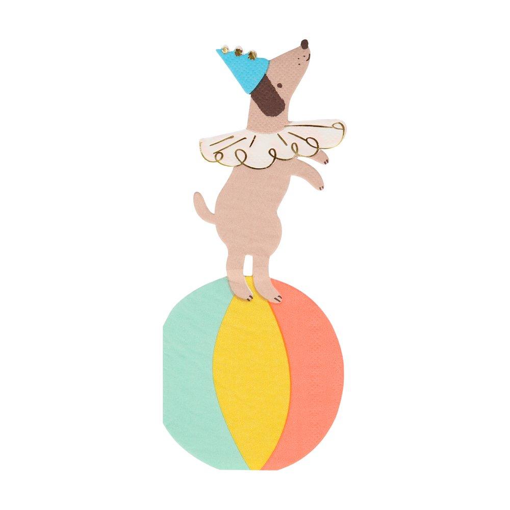 A die-cut paper napkin illustration of a dog balancing on a colorful ball, wearing a party hat with gold foil detail.