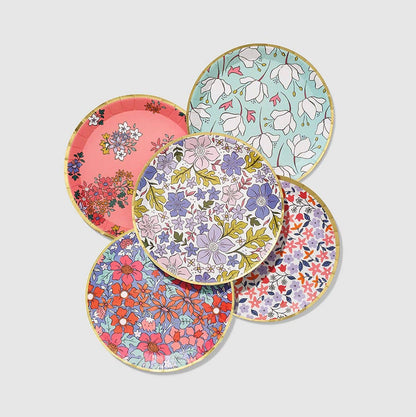 A set of small round paper plates with various floral patterns and a gold rim.