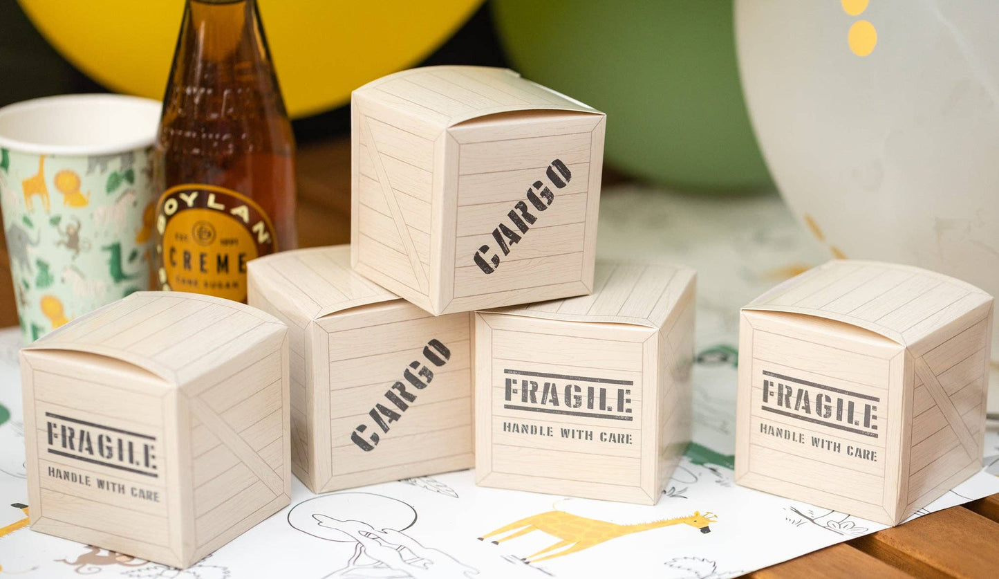 A set of beige wooden cargo box treat containers with black text 'CAROGO' and 'FRAGILE' printed on the lids, placed on a surface with safari party-related items in the background.