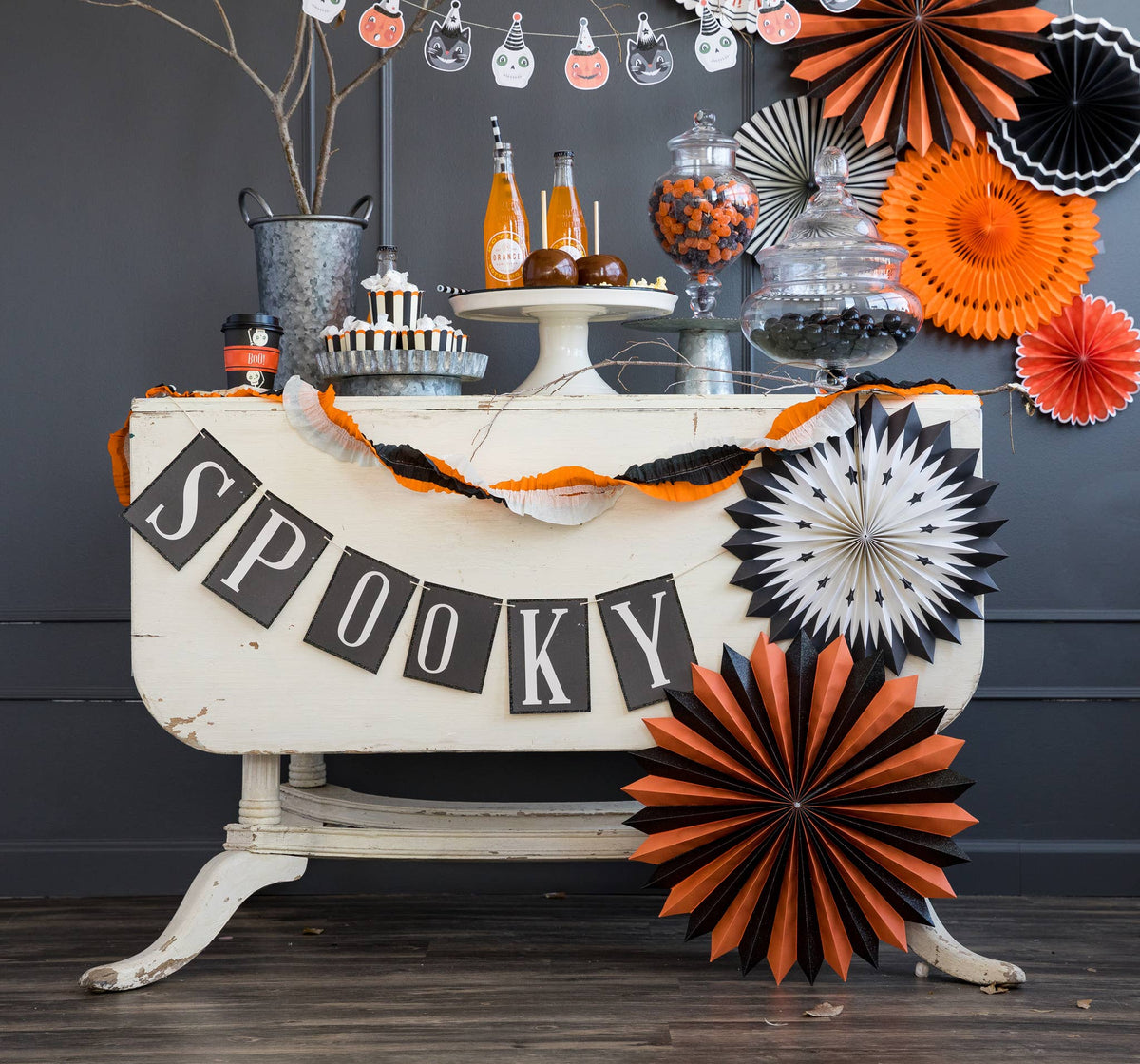 A 'SPOOKY' word banner with black glitter accents, designed for Halloween decorations, displayed over a table with themed items.