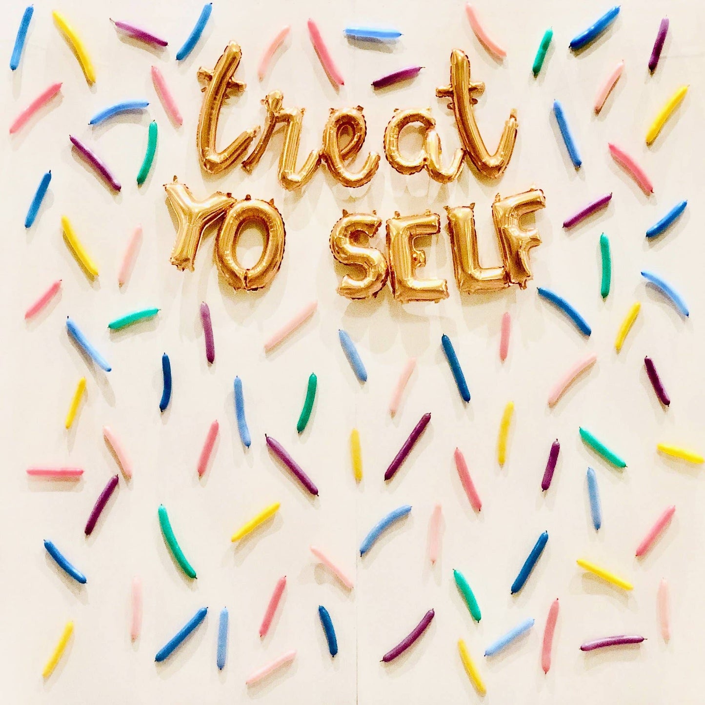 A wall decorated with multicolored latex balloons arranged in a pattern that spells out 'TREAT YO SELF' with each letter represented by a different color.