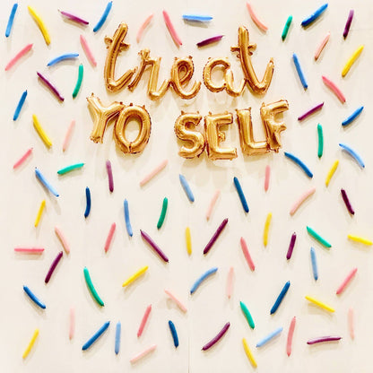 A wall decorated with multicolored latex balloons arranged in a pattern that spells out 'TREAT YO SELF' with each letter represented by a different color.